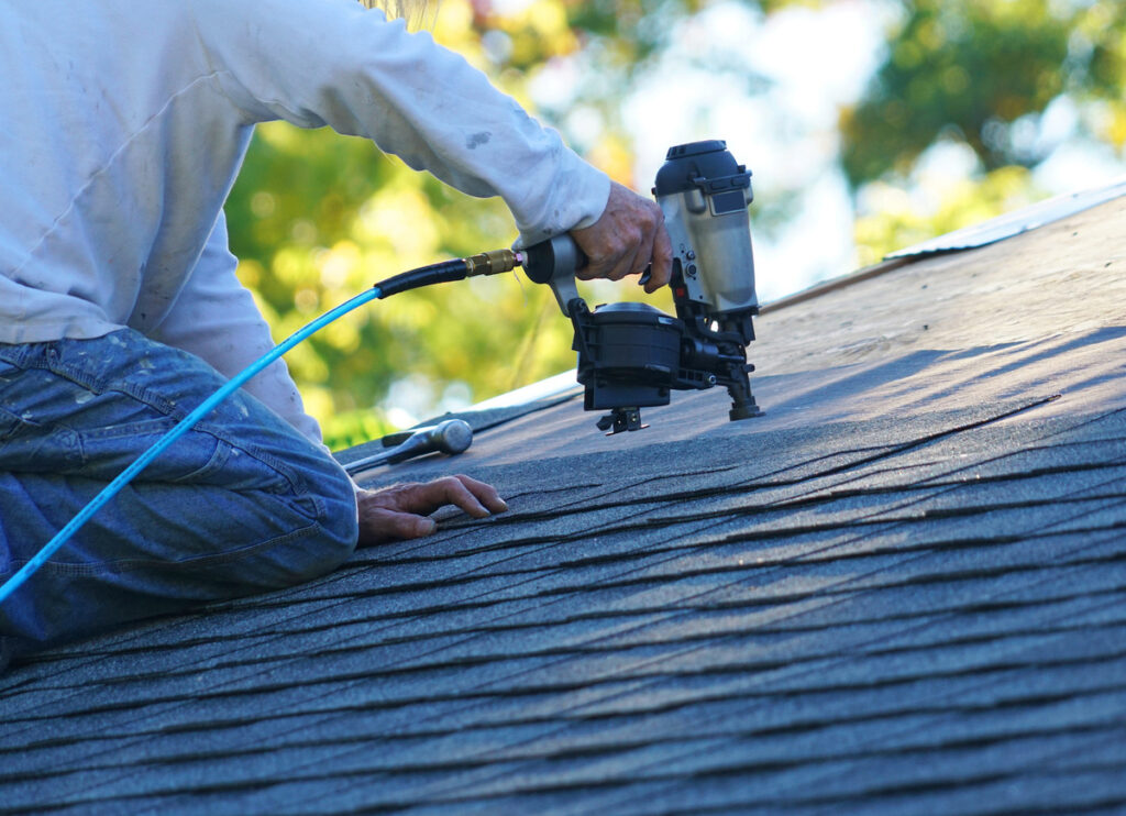handyman using nail gun to install shingle to repair roof