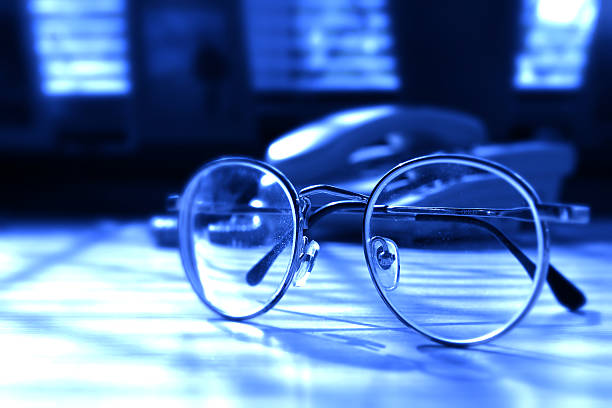 A pair of glasses on a desk with telephone in bg