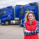 Portrait of female truck driver standing by trucks at truck stop.