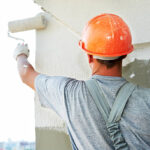 Young painting facade builder worker with roller at thermal insulation works