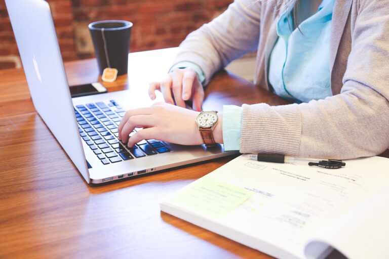 A close-up of a student’s hands typing on a laptop next to a notebook and tea, representing personalized academic writing assistance for research and essay composition.