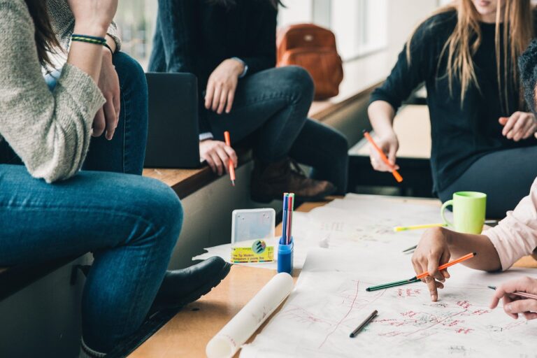 A group of university students collaborating on a large paper mind map using colorful pens, demonstrating collaborative study hacks for students in a classroom setting.