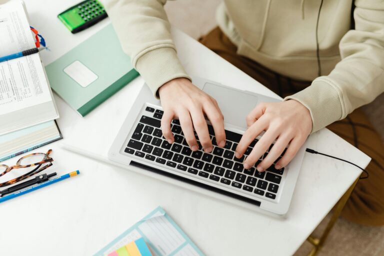 A student typing on a laptop at a clean white desk with study materials, representing how assignment help services can assist with digital coursework and essay writing.