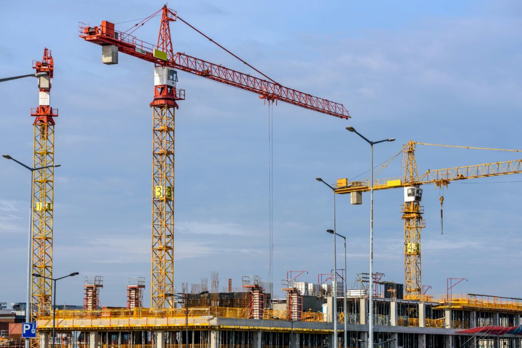 Three tall tower cranes and scaffolding at a busy job site managed by a Construction Company London, set against a blue sky.