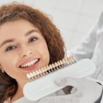 Woman smiling while male dentist keeping teeth color range