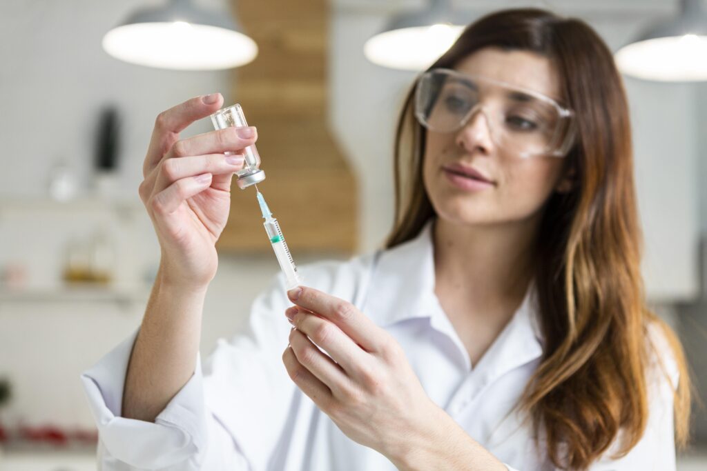 female-scientist-with-safety-glasses-holding-syringe-with-vaccine-lab