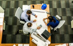 An overhead view of a team collaborating on blueprints, illustrating the real-world scenarios covered in project management assignment help.