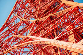 A low-angle view of a complex red steel lattice tower against a blue sky, illustrating heavy superstructure construction engineering. Caption: Intricate steel frameworks are a defining feature of