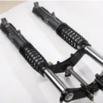 Pair of black and silver front suspension shock absorbers with coil springs, connected by a metal linkage, placed on a white surface.