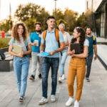 A diverse group of international students walking and talking on a modern UK university campus, carrying notebooks and tablets during sunset, illustrating how to adapt to UK student life.