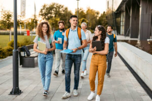 A diverse group of international students walking and talking on a modern UK university campus, carrying notebooks and tablets during sunset, illustrating how to adapt to UK student life.
