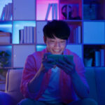 asian man plays mobile games on sofa in the evening at home