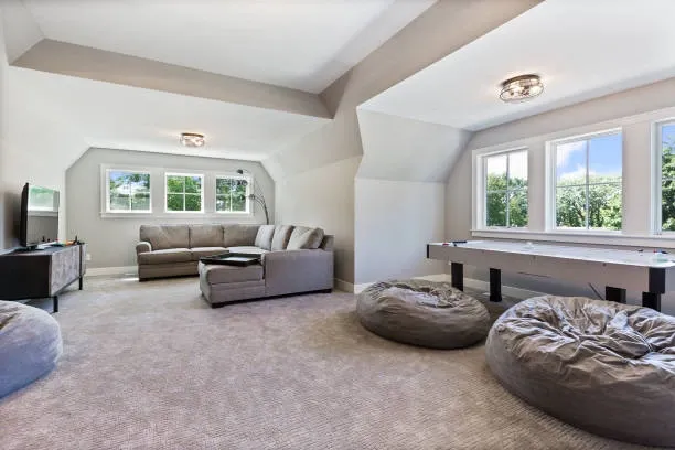 A spacious, carpeted multi-purpose room created through a garage conversion, featuring a large sectional sofa, bean bags, and an air hockey table under a vaulted ceiling.