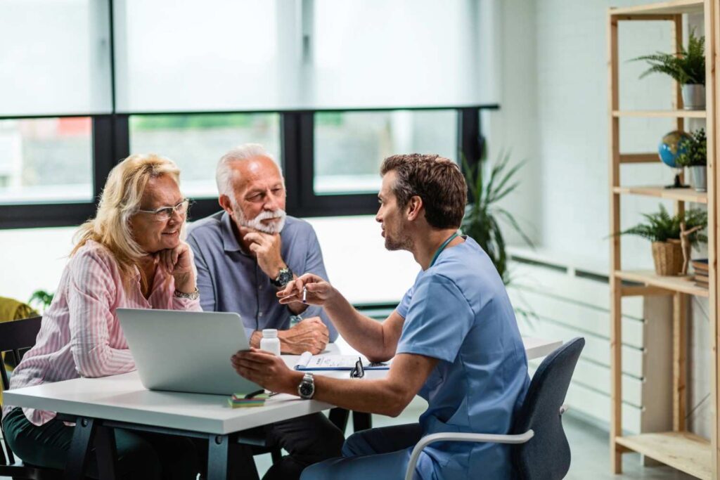 happy-mature-couple-their-doctor-communicating-while-using-laptop-medical-appointment