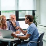 happy-mature-couple-their-doctor-communicating-while-using-laptop-medical-appointment