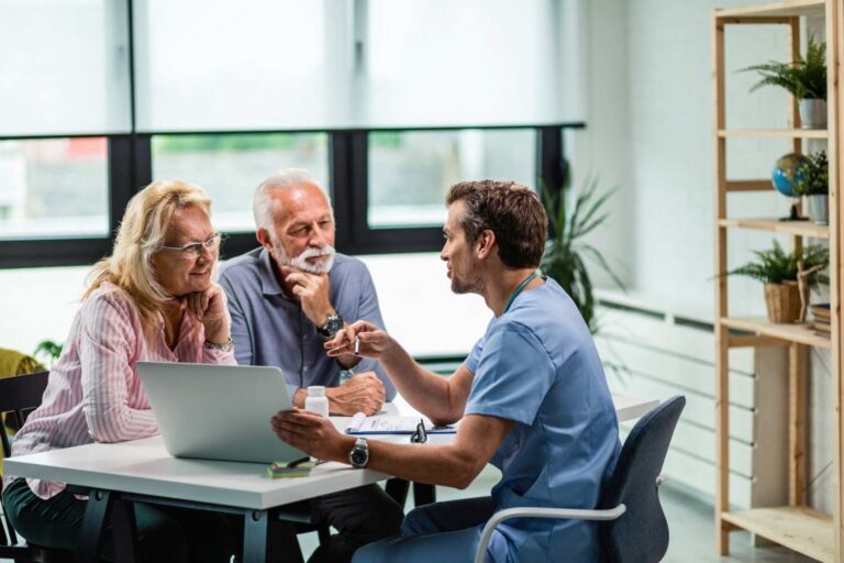 happy-mature-couple-their-doctor-communicating-while-using-laptop-medical-appointment