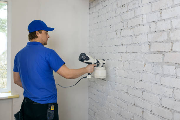 man painting old brick wall in white color with paint sprayer