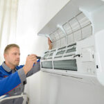 Young Man Repairing Air Conditioner Standing On Stepladder