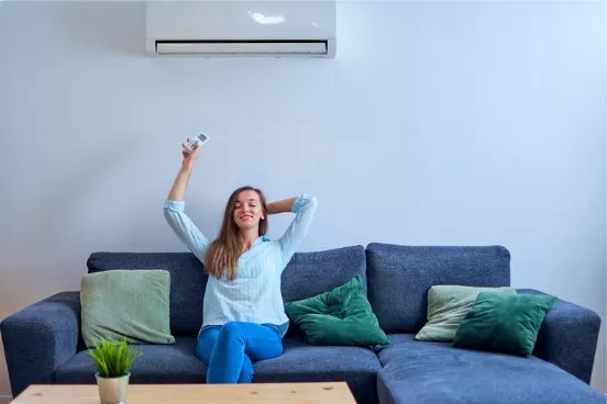 young-happy-woman-with-closed-eyes-sitting-on-sofa-under-air-conditioning-and-adjusting