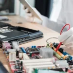 Technician testing a computer motherboard with a multimeter probe during laptop repair and electronic hardware diagnostics.